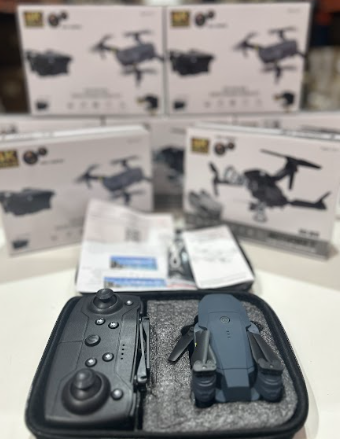 Dron doble cámara 4K con control remoto y cajas de presentación en el fondo.